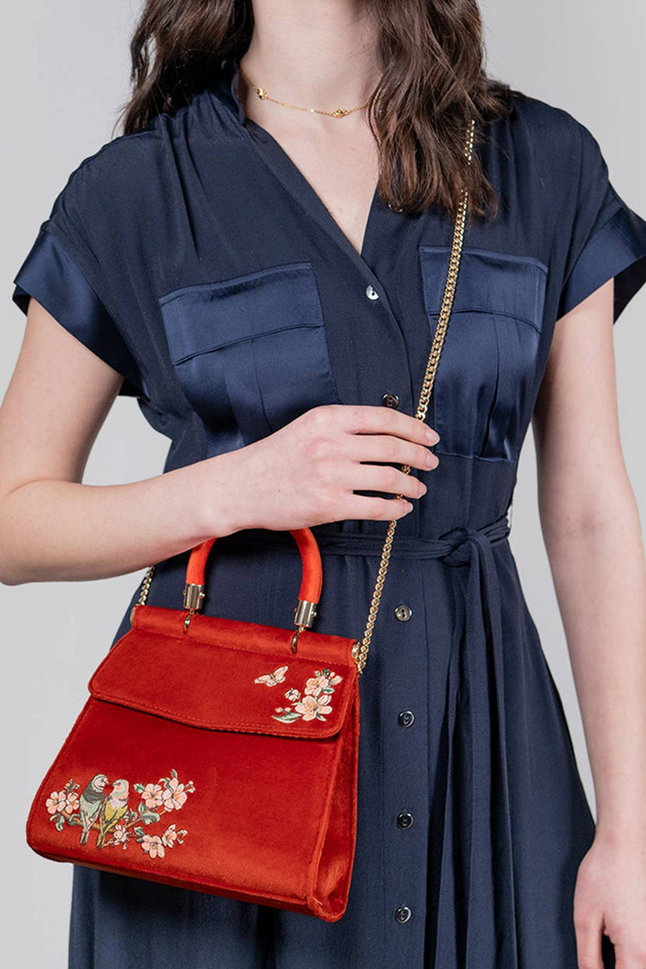 Woman holding a red handbag with floral embroidery against a plain background
