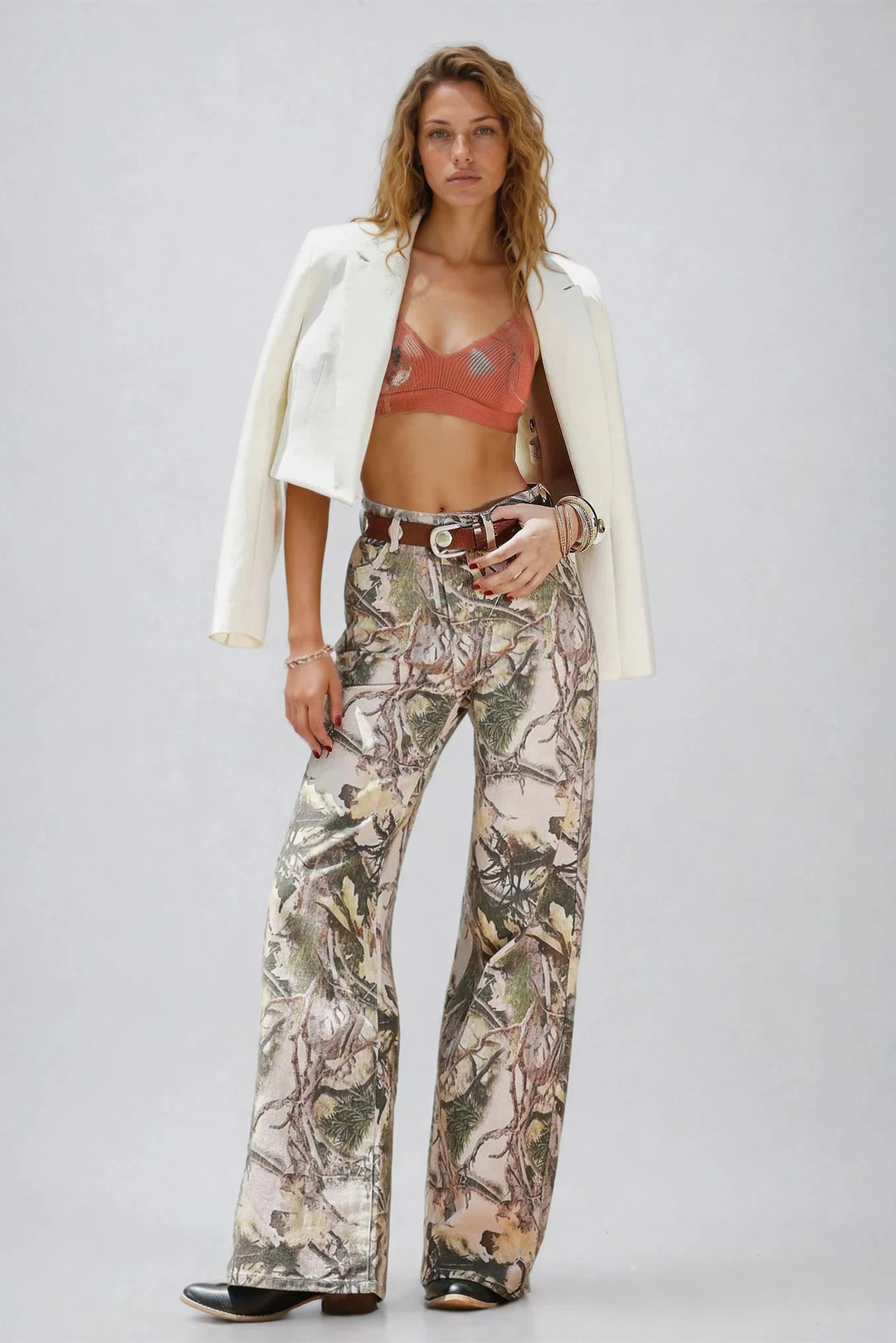 Woman wearing a white blazer, red bralette, and camouflage pants on a plain background