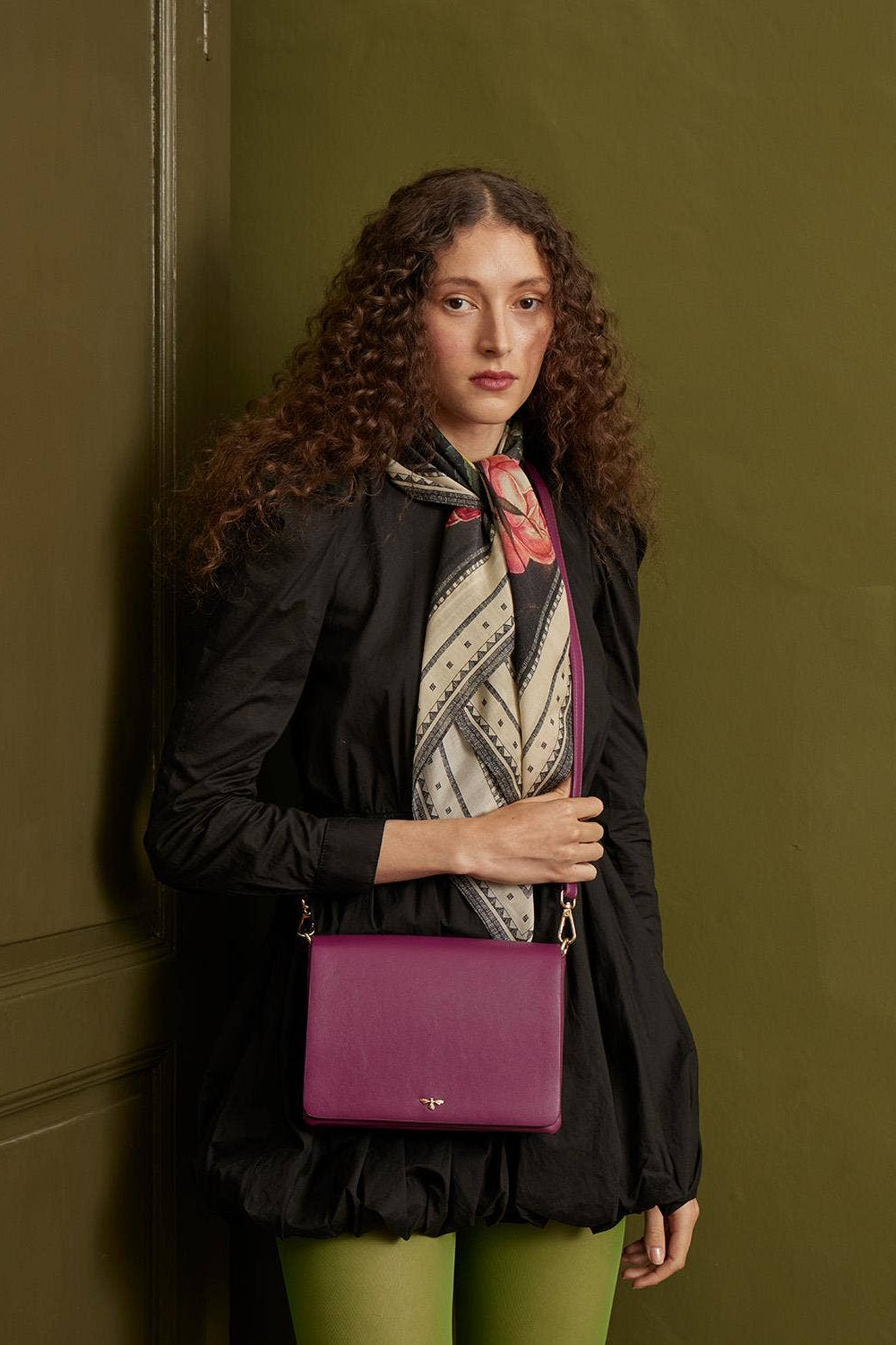 Woman holding a purple handbag against a green wall