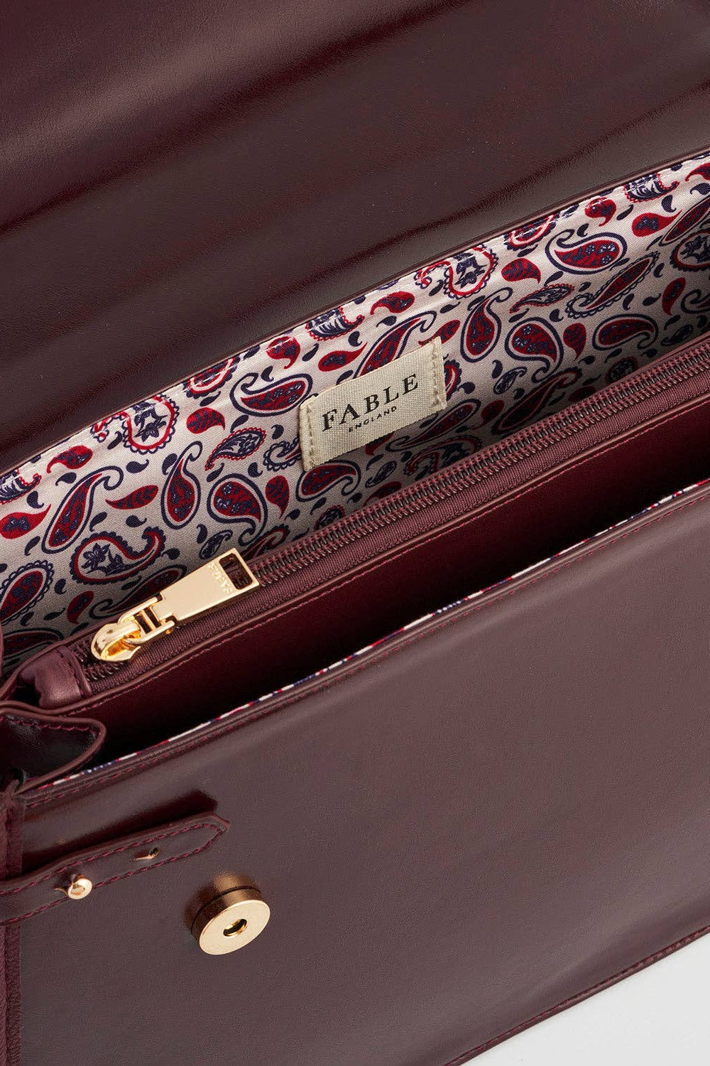 Close-up of a brown leather bag with a paisley patterned strap, featuring the brand 'Fable'.