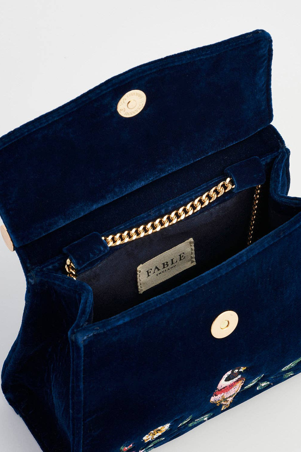 Navy blue velvet handbag with gold accents and 'Fable' branding on a light gray background