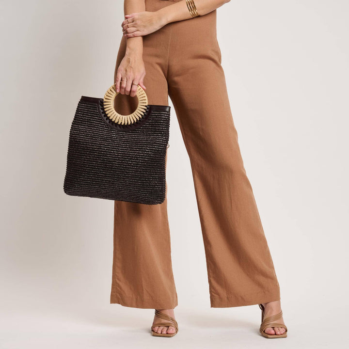 Person holding a black woven handbag with a beige handle against a neutral background