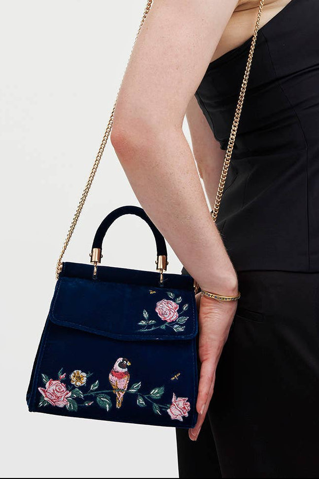Woman holding a navy handbag with floral embroidery against a plain background