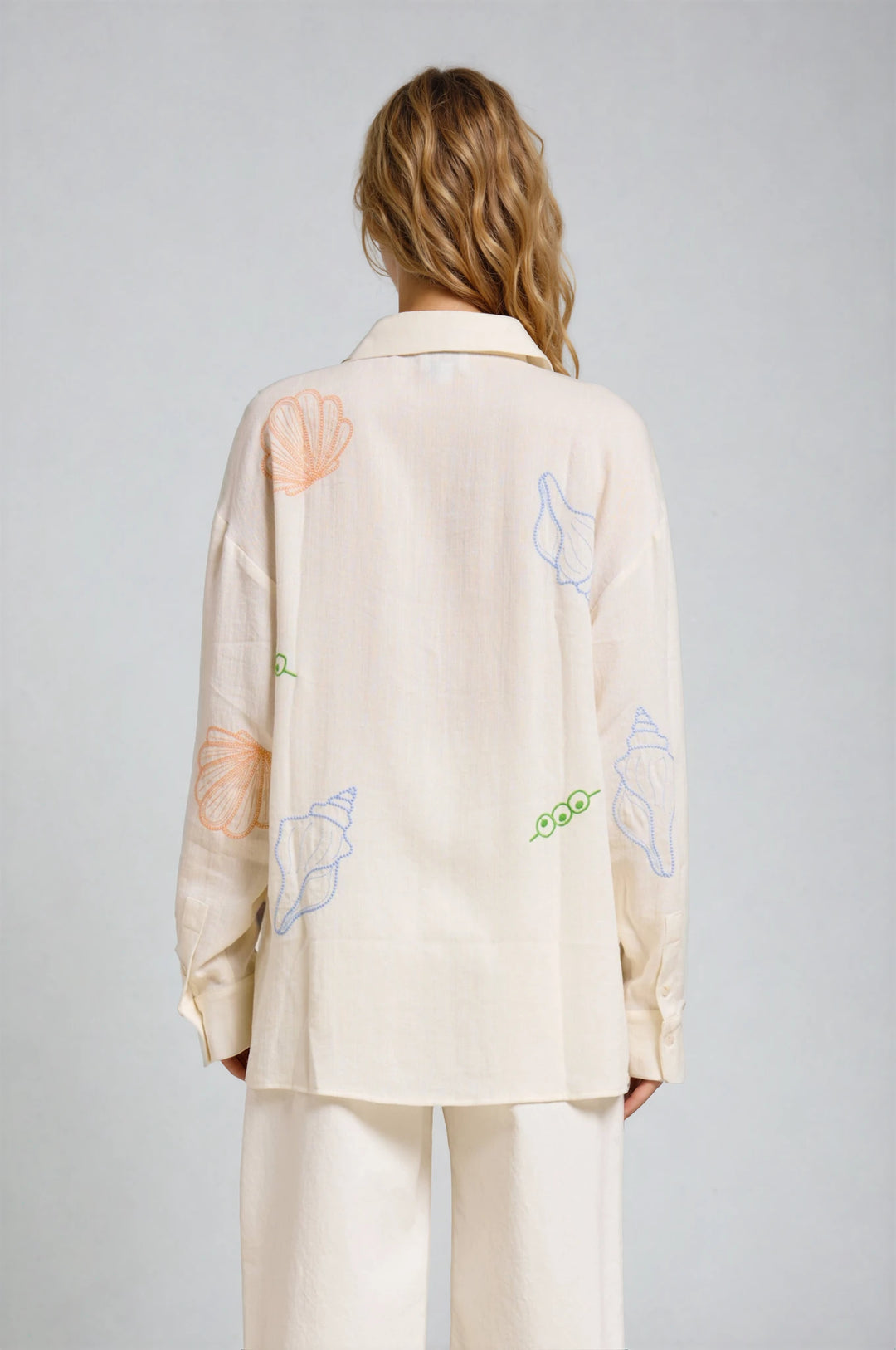 Person wearing a beige outfit with embroidered designs on a plain background