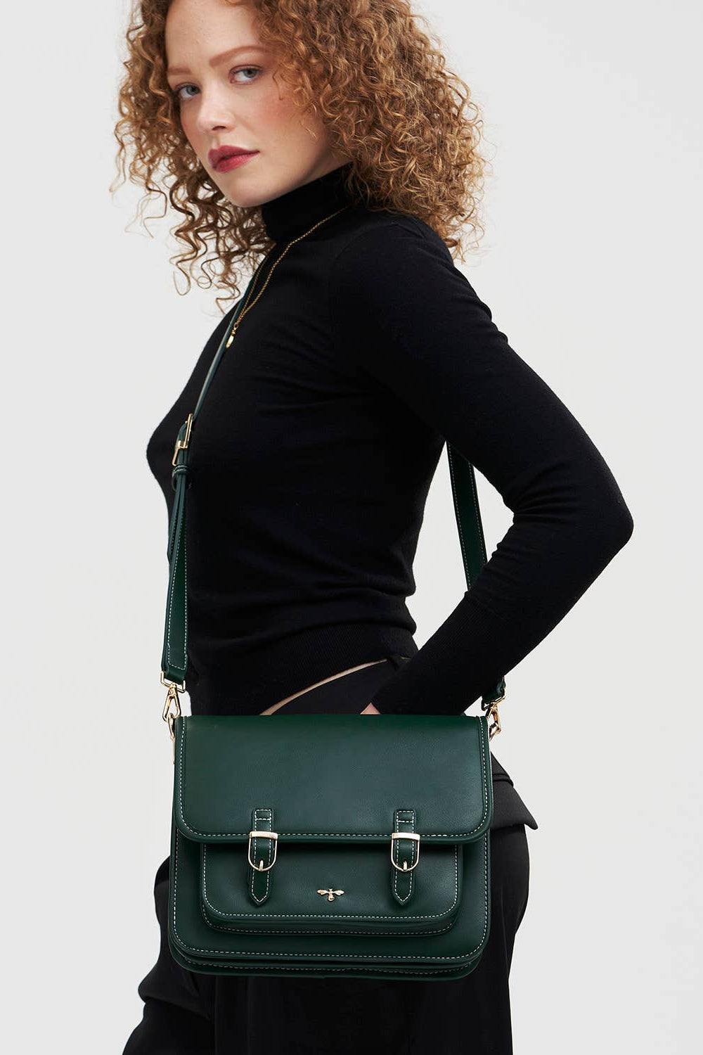 Woman holding a green handbag against a plain background