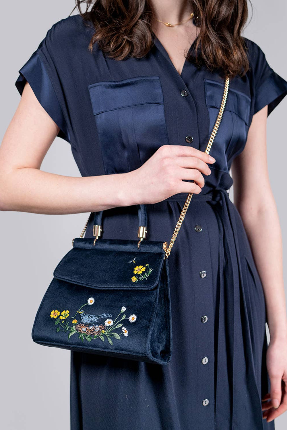 Person wearing a navy blue dress holding a matching embroidered handbag against a gray background