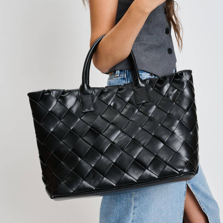 Black woven handbag held by a person against a neutral background