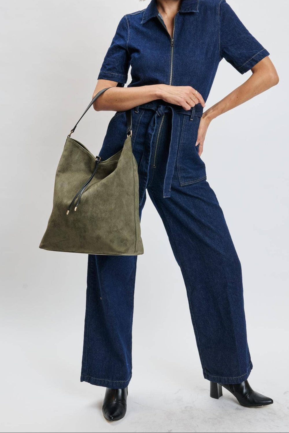 Woman wearing a blue jumpsuit holding a green bag on a white background
