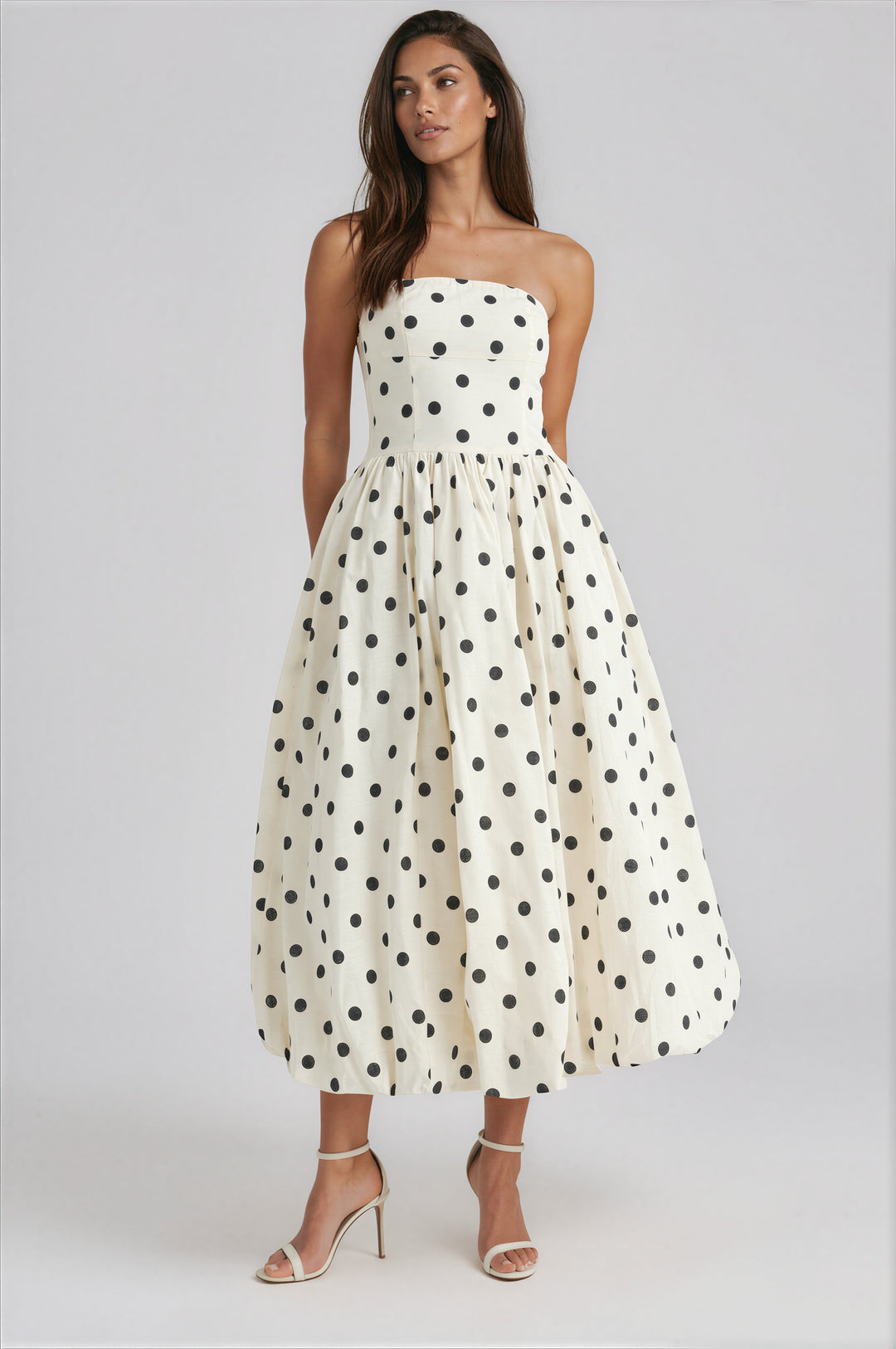 Woman wearing a strapless polka dot dress on a white background