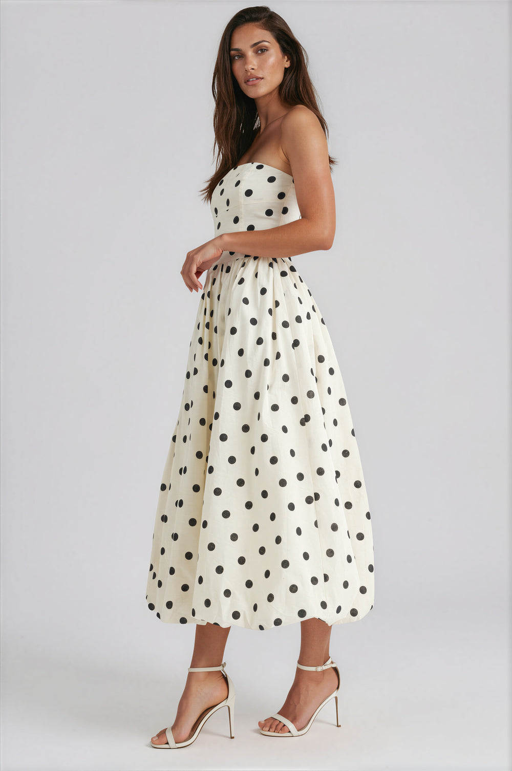 Woman wearing a white strapless dress with black polka dots on a white background