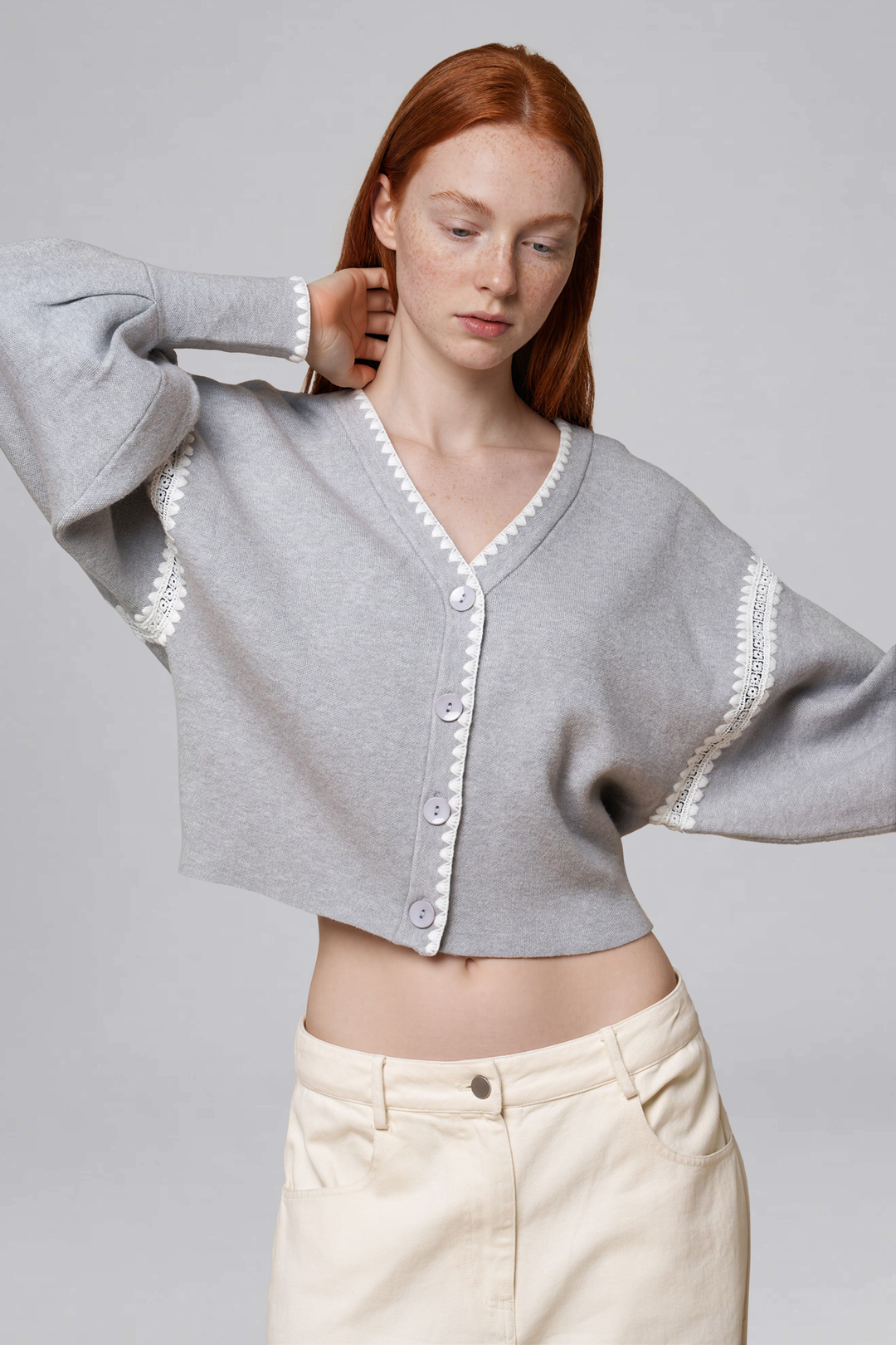 Grey cropped button-front cardigan with white lace trim and a V-neckline, front view