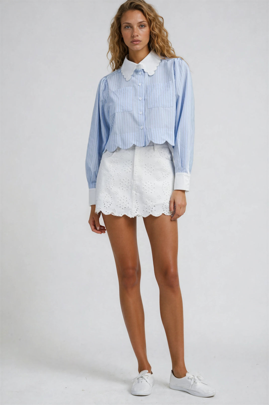 Woman wearing a blue striped shirt and white shorts on a plain background