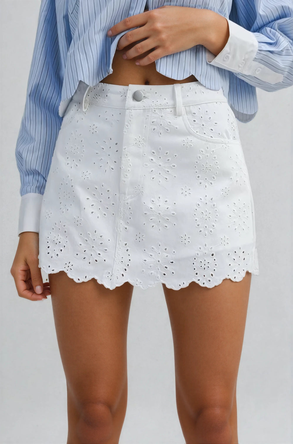 White eyelet skirt worn with a blue striped shirt on a plain background