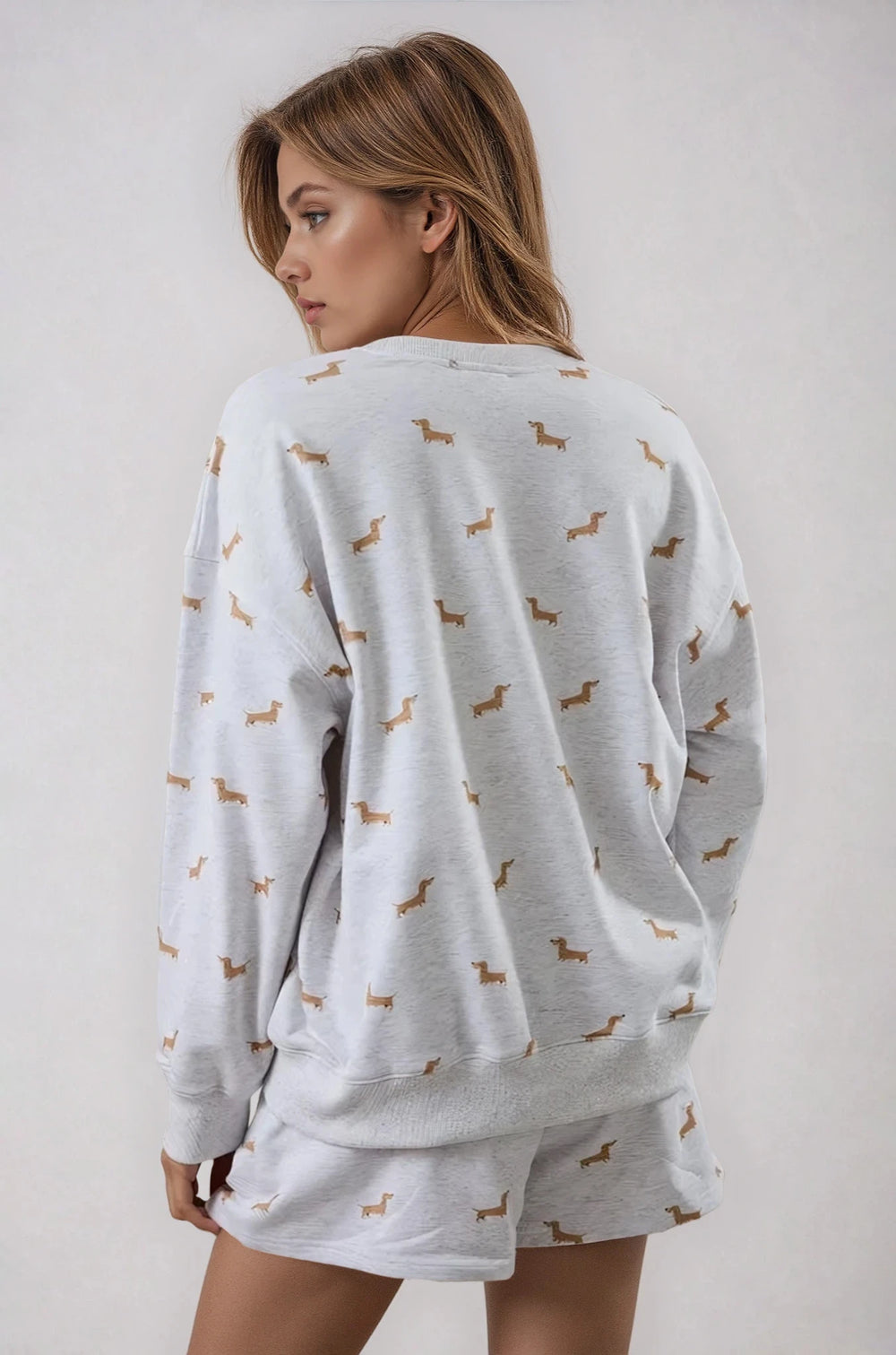 Woman wearing a light gray pajama set with dachshund pattern on a plain background