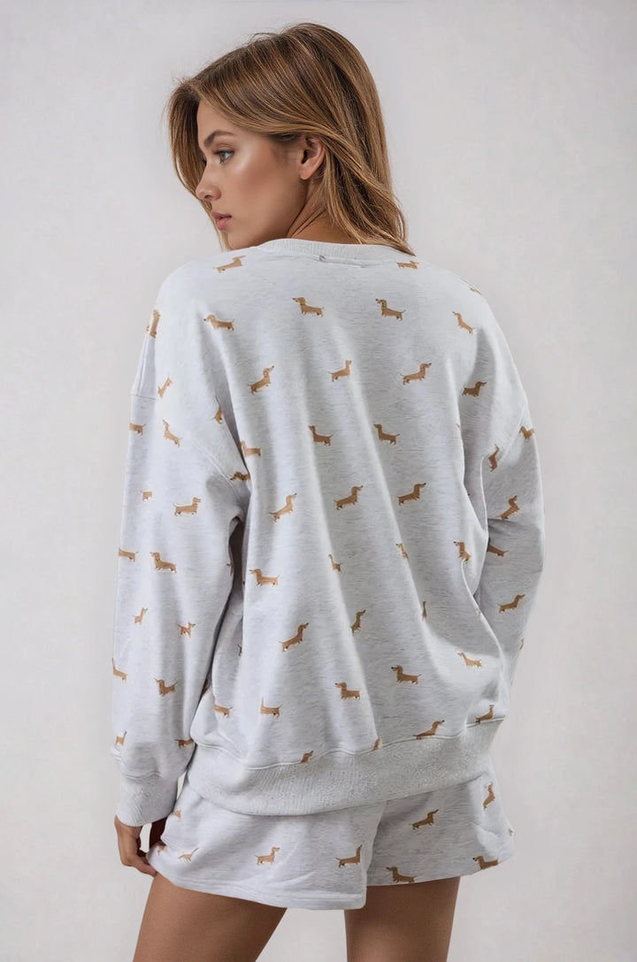 Woman wearing a light gray pajama set with dachshund pattern on a plain background