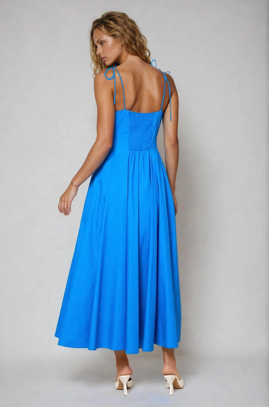 Woman wearing a blue dress with thin straps on a plain background