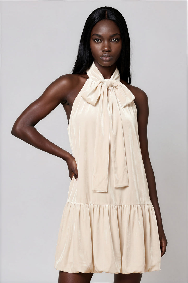 Woman wearing cream velvet sleeveless mini dress with mock neck bow and bubble hem