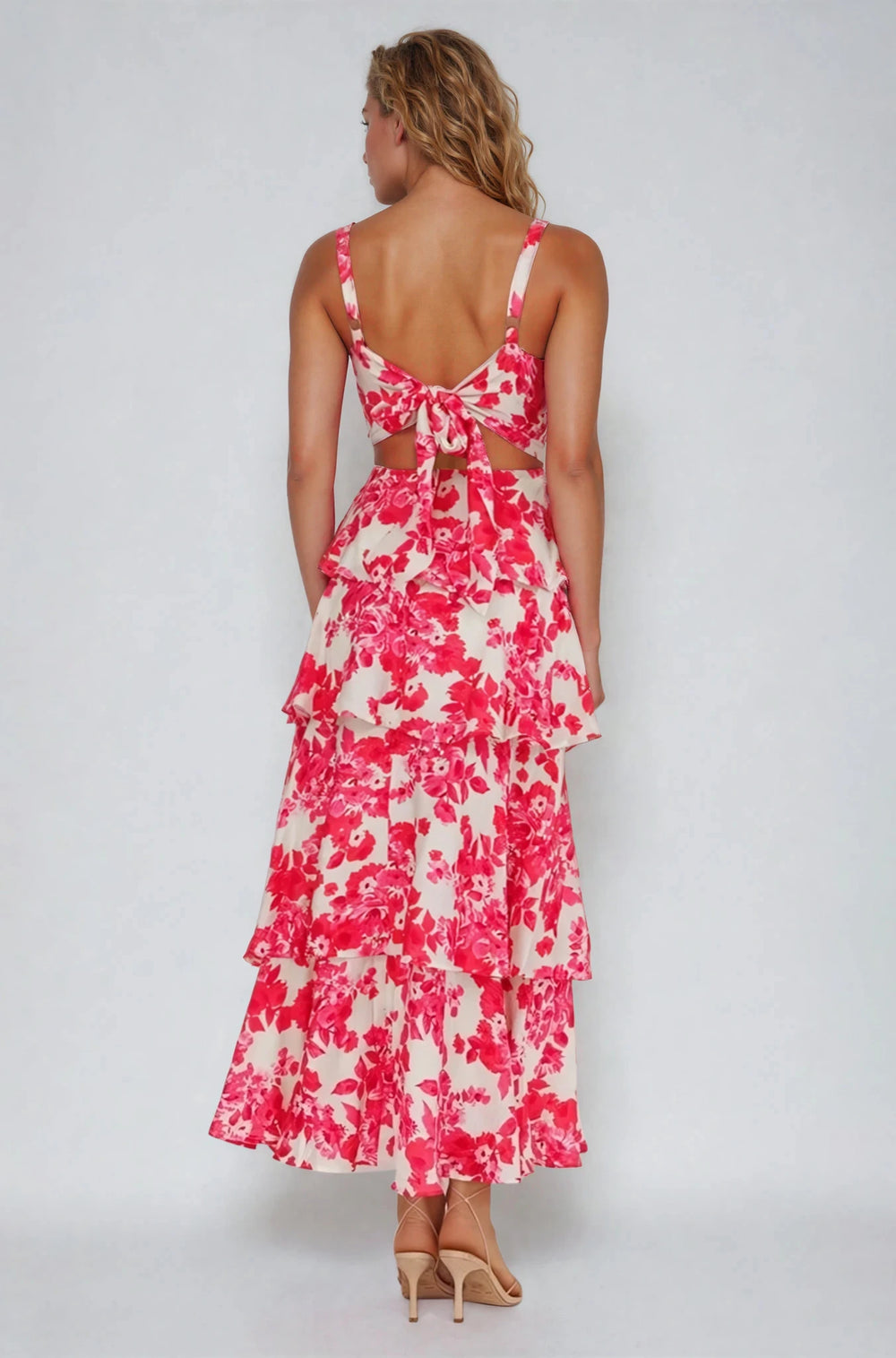 Woman wearing a pink and white floral dress with cut-out back on a gray background