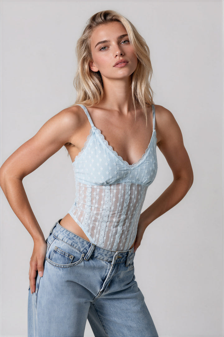 Model wearing the Gia Bodysuit in powder blue, a semi-sheer floral lace bodysuit with a scalloped V-neckline and thin adjustable straps, styled with light wash jeans
