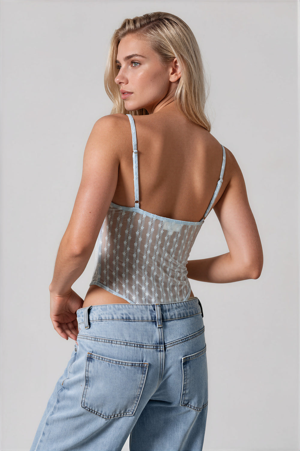 Side view of the Gia Bodysuit in powder blue, showing the semi-sheer lace body and scalloped neckline, styled with light wash jeans