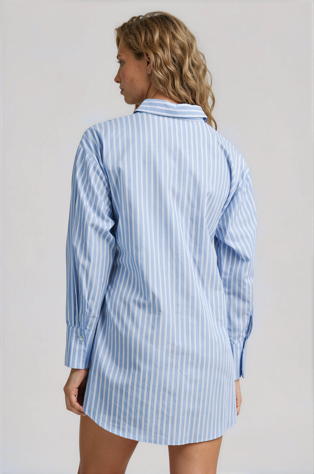Woman wearing a blue and white striped shirt dress against a gray background