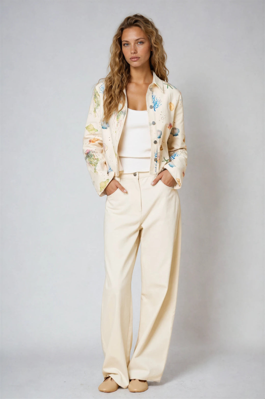 Woman wearing a cream-colored outfit with floral embroidery on a plain background