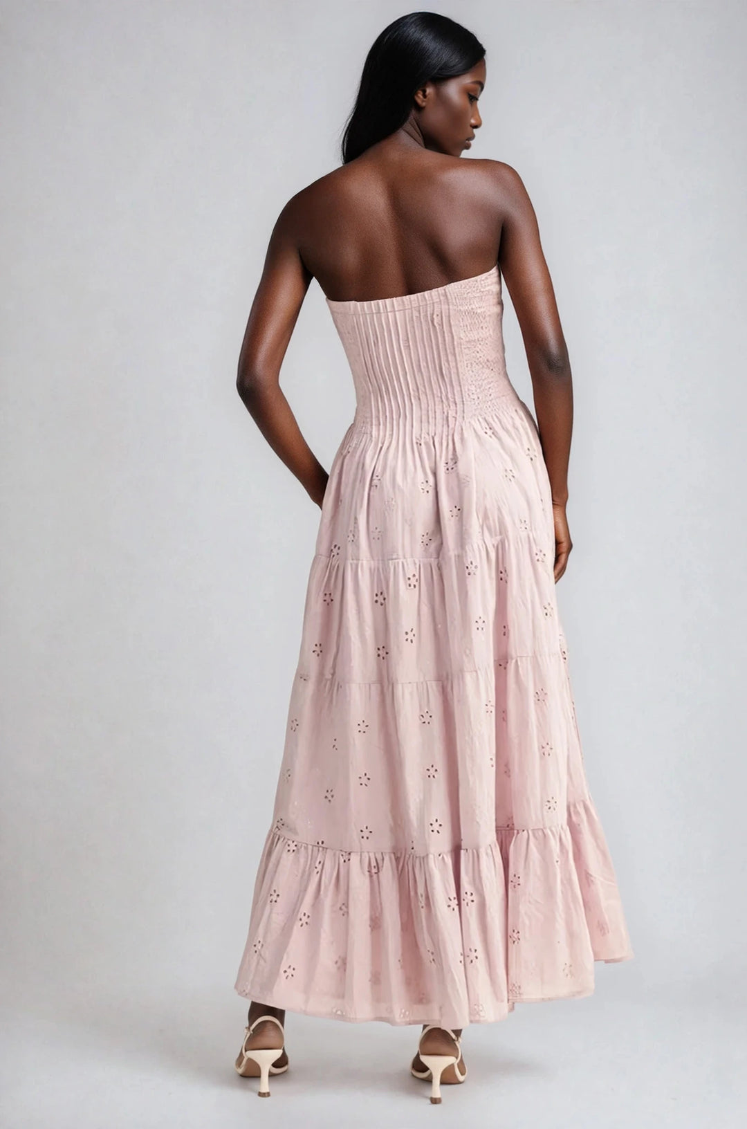 Woman wearing a pink strapless dress with floral embroidery on a plain background