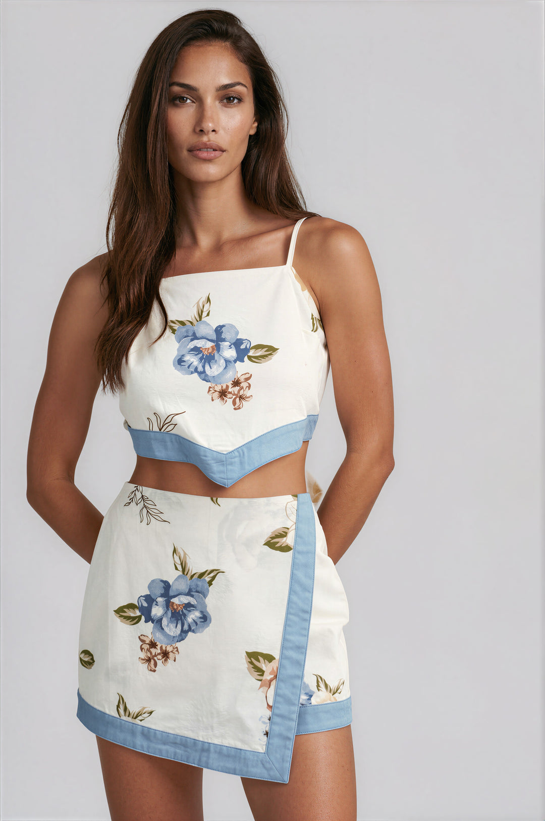 Woman wearing the Honey Floral Skort Set, a cream two-piece with blue floral print and blue contrast trim, featuring a cropped cami top and high-waisted wrap mini skort.