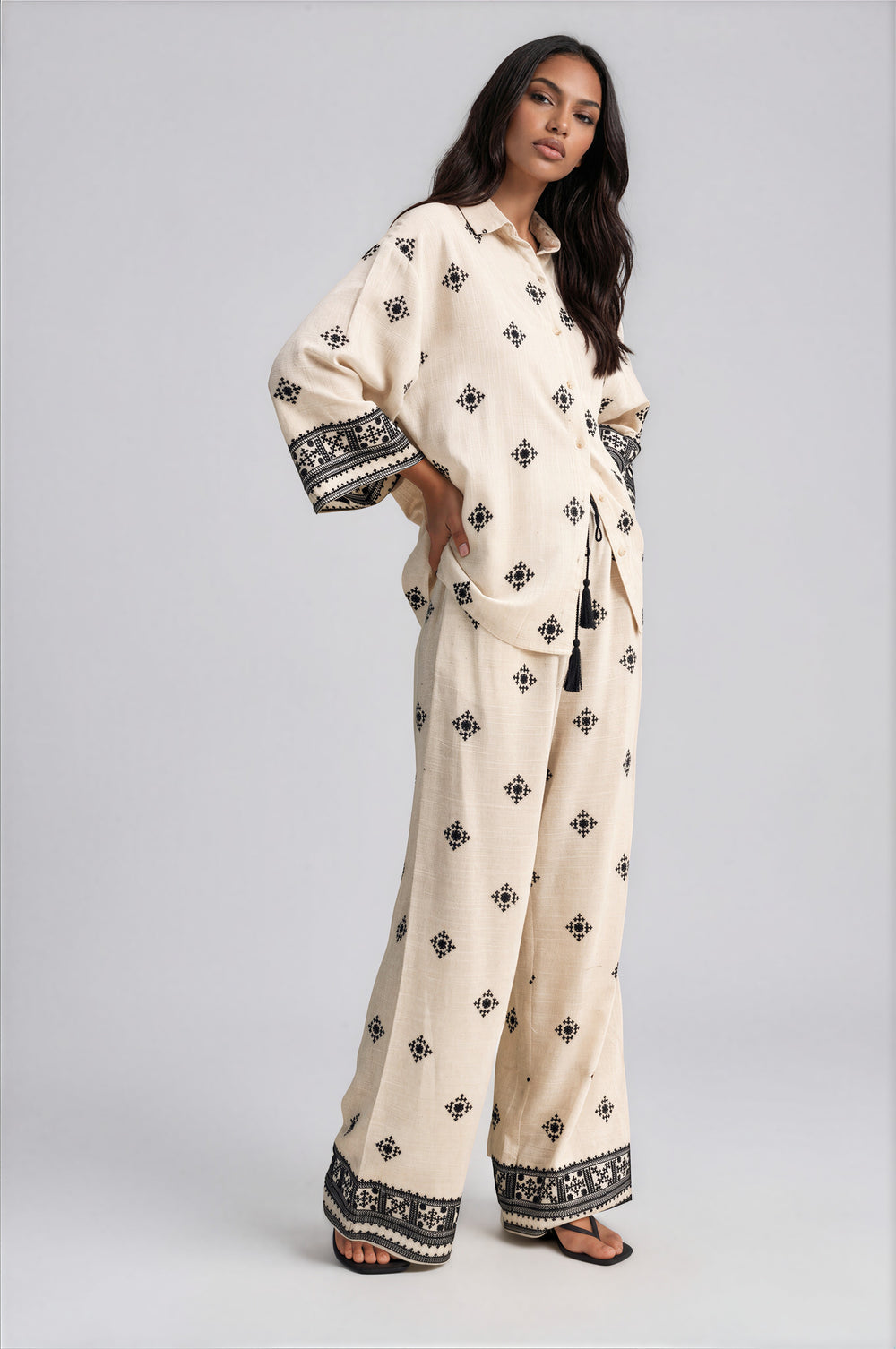 Side view of cream embroidered wide leg pants set with oversized collared top and tassel tie waist