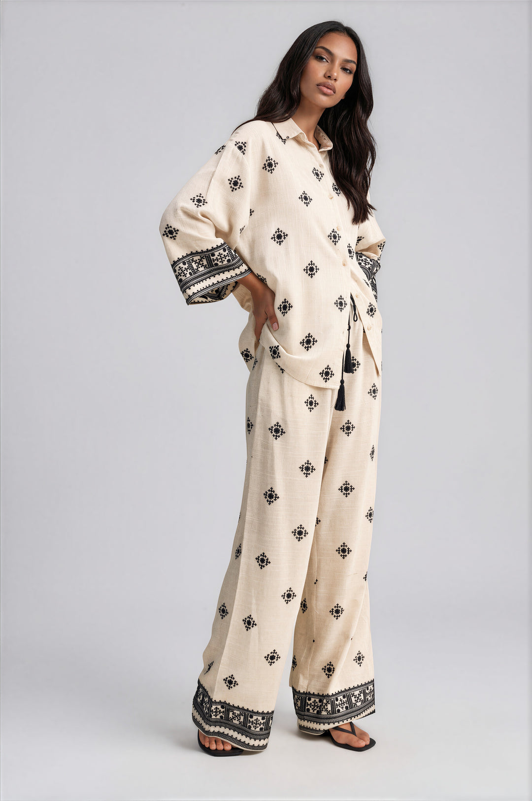 Side view of cream embroidered wide leg pants set with oversized collared top and tassel tie waist