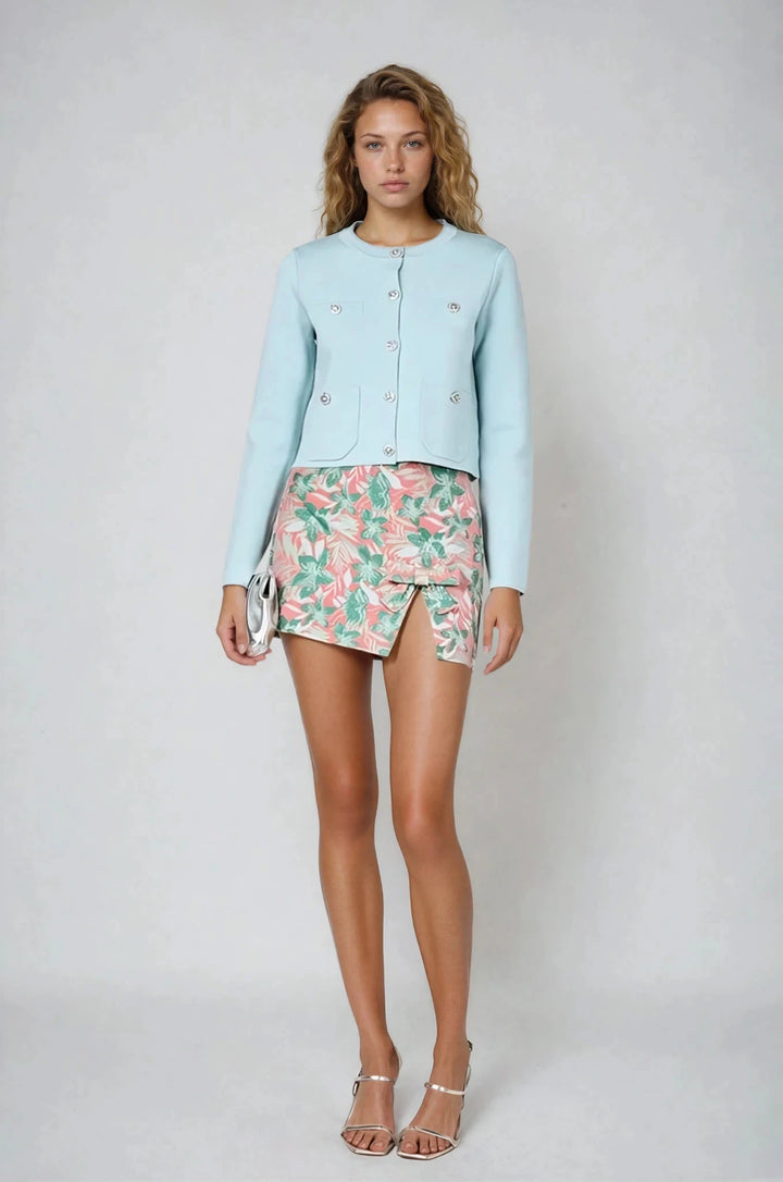 Woman wearing a light blue jacket and floral skirt on a white background