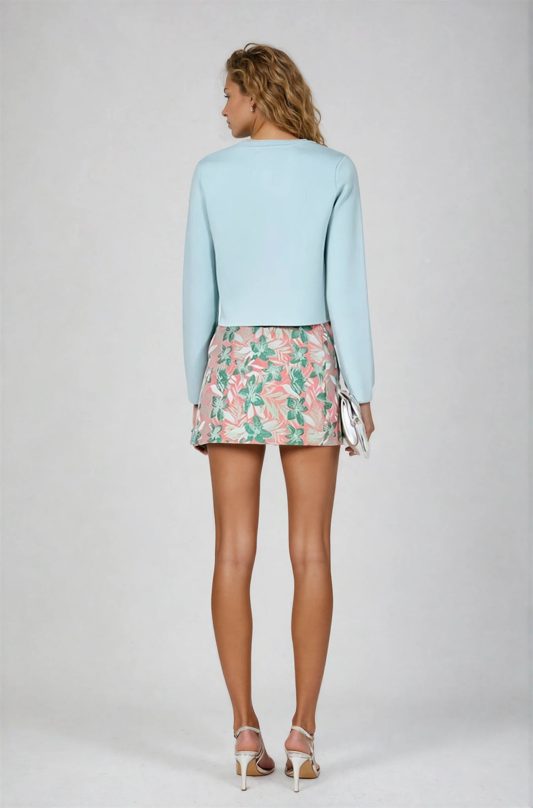 Woman wearing a light blue sweater and floral skirt on a plain background