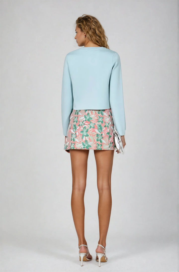 Woman wearing a light blue sweater and floral skirt on a plain background