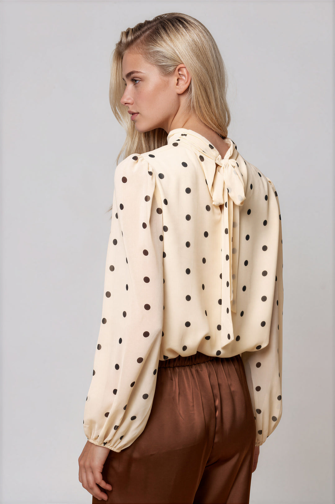 Back view of cream polka dot blouse with self-tie bow neckline and puff sleeves