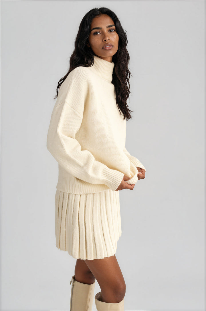 Cream oversized turtleneck sweater with a matching pleated knit mini skirt