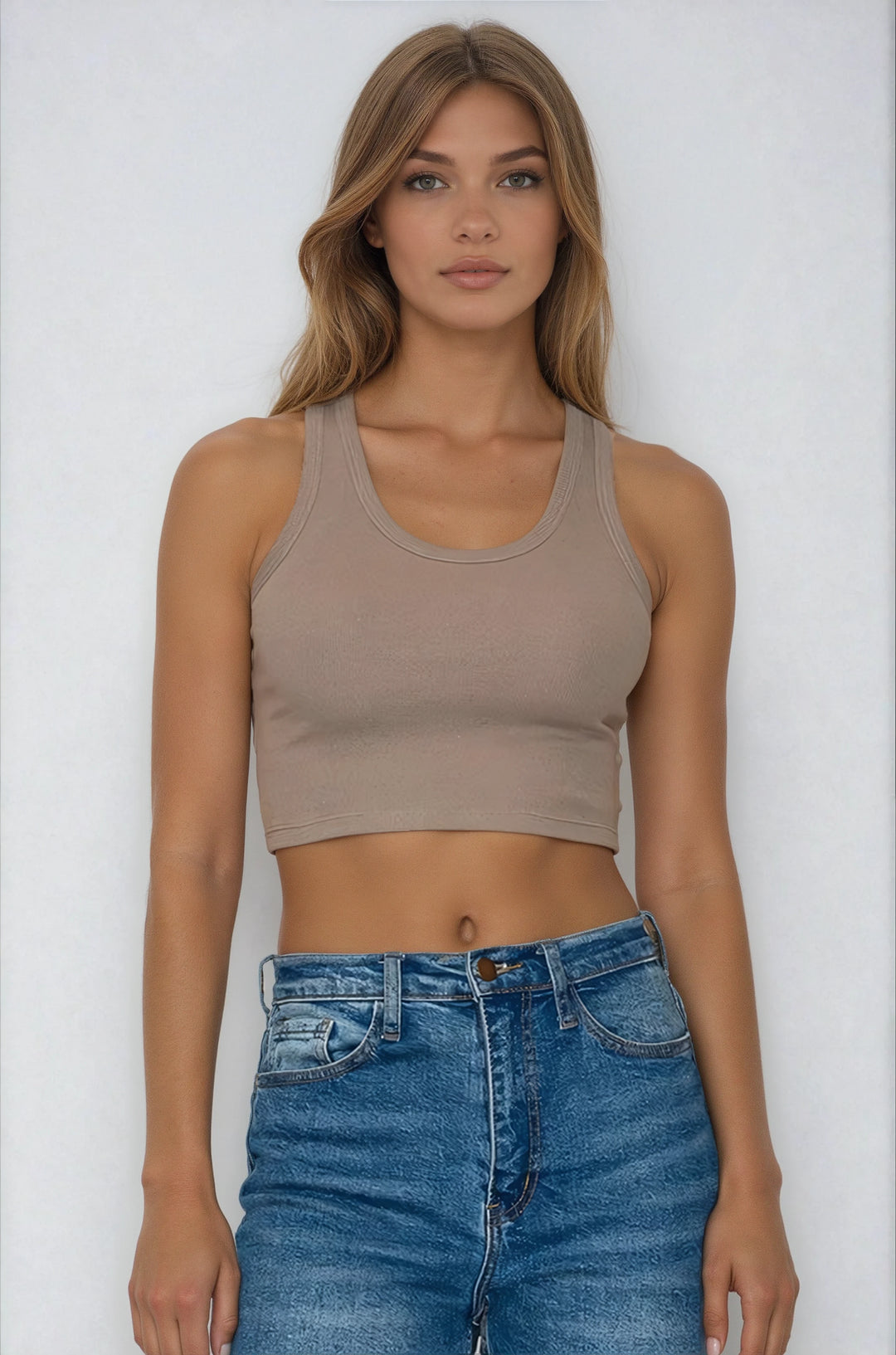 Woman wearing a beige crop top and blue jeans against a white background