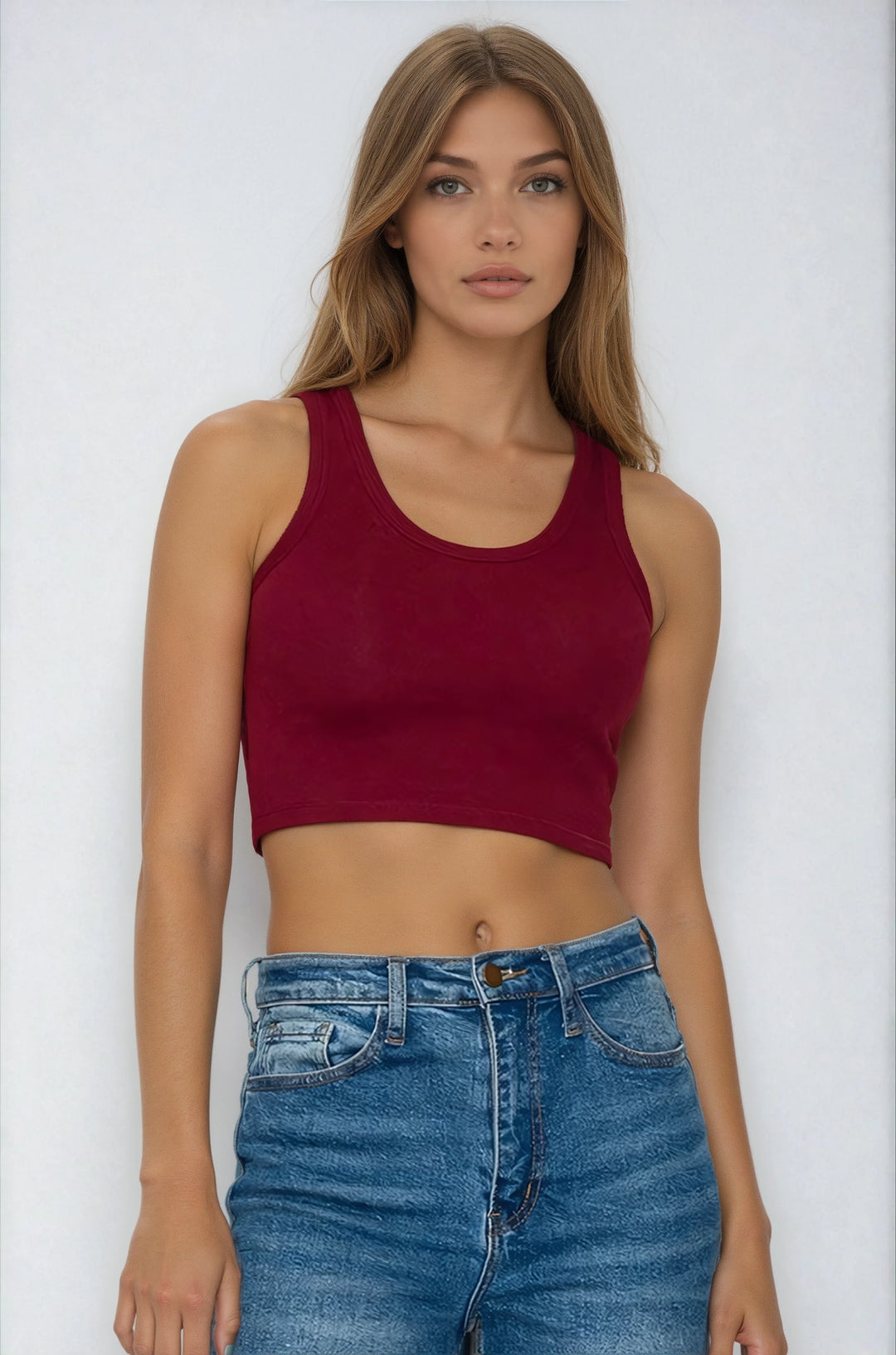 Woman wearing a red tank top and blue jeans against a white background