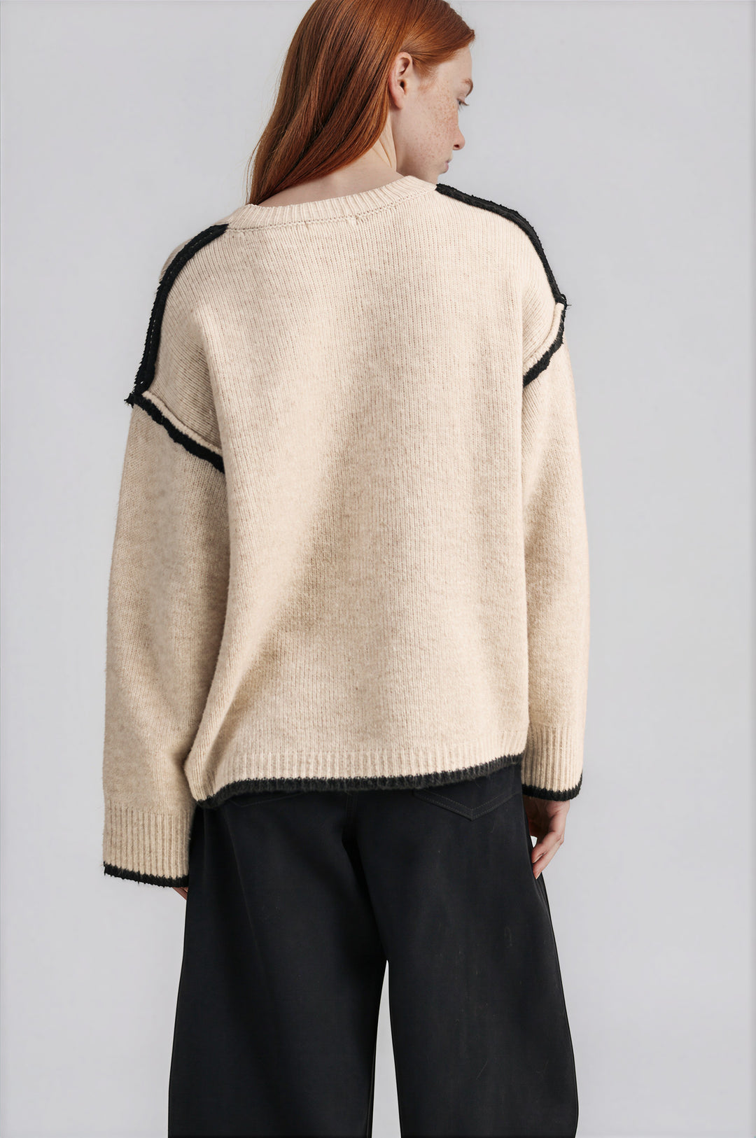 Detail of black contrast trim and exposed seams on cream knit sweater