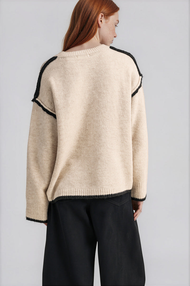 Detail of black contrast trim and exposed seams on cream knit sweater