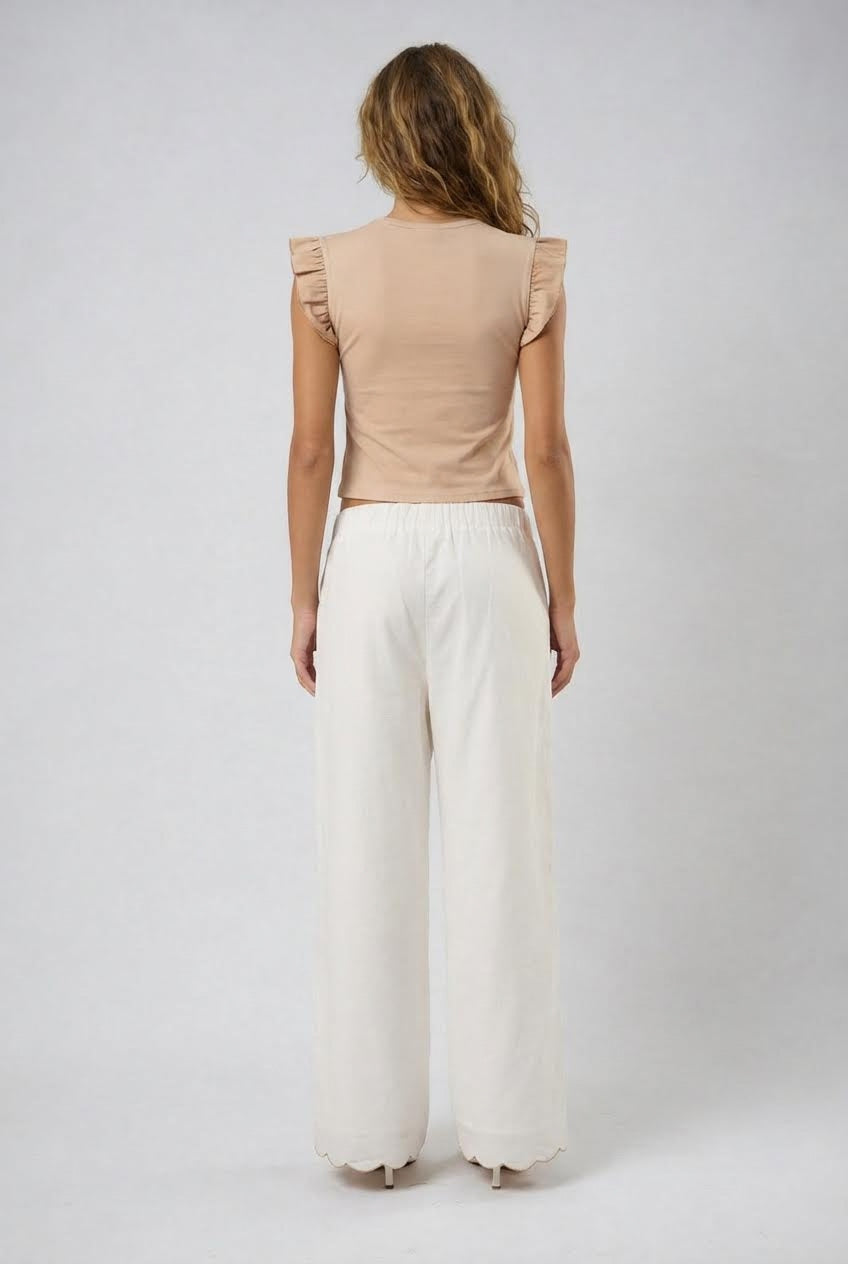 Woman wearing a beige top and white pants on a plain background