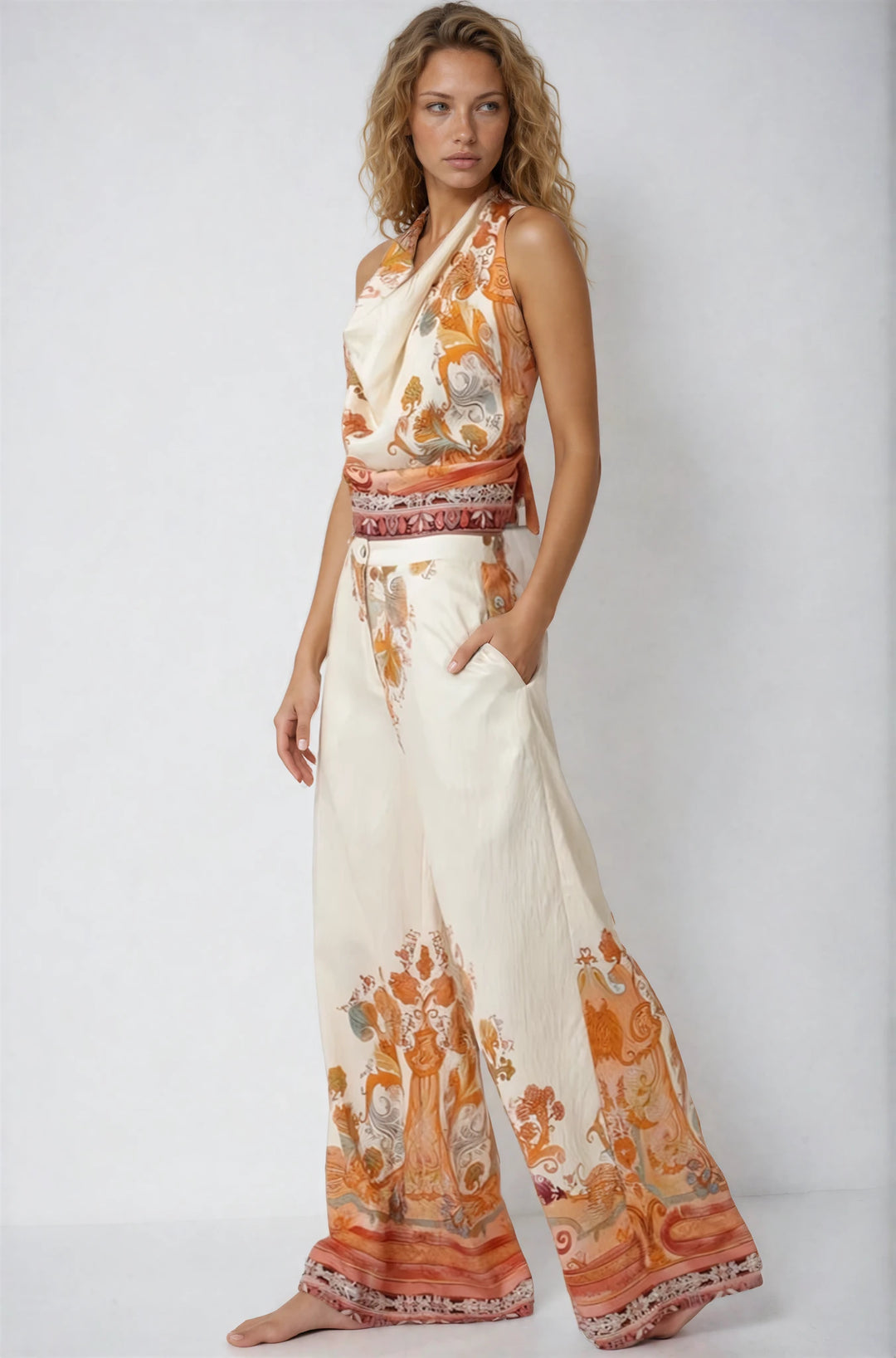 Woman wearing a sleeveless top and wide-leg pants with orange and white pattern on a plain background