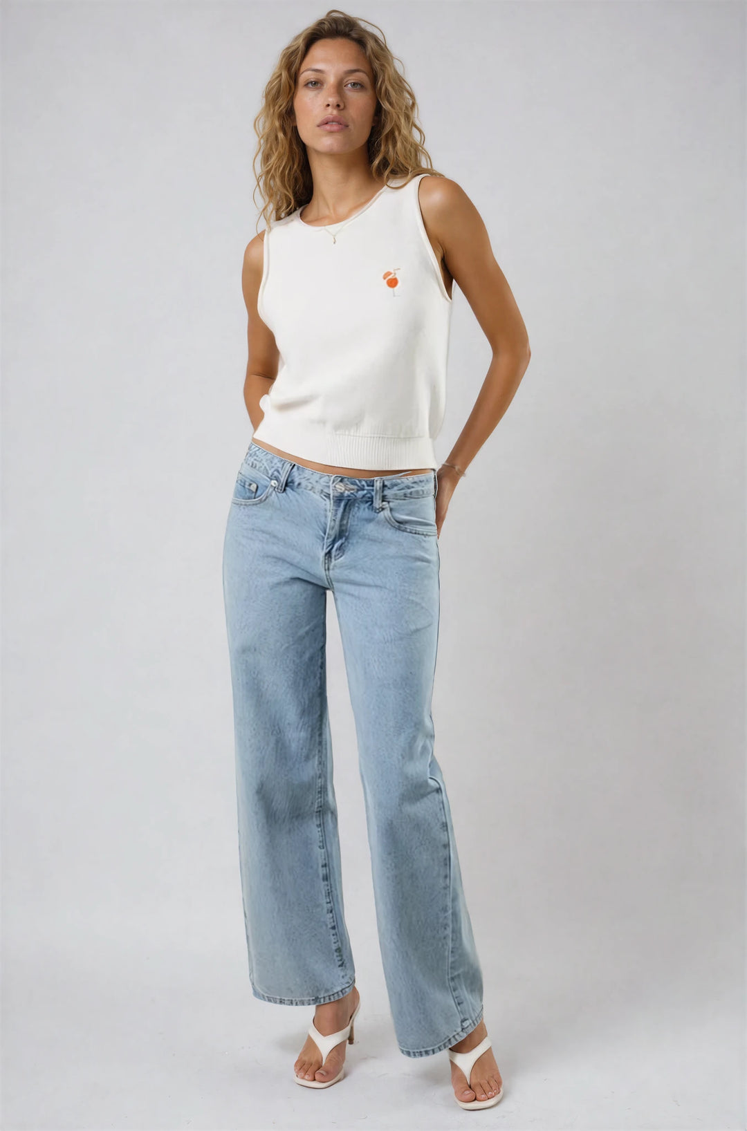 Woman wearing a white sleeveless top and light blue jeans on a plain background