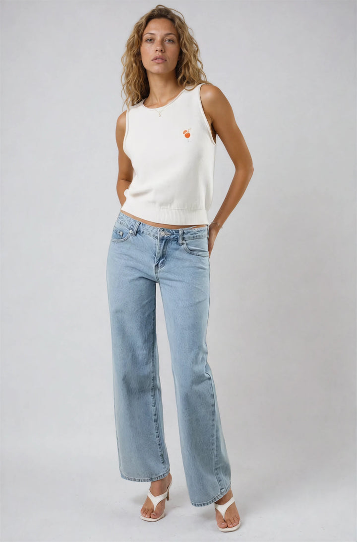 Woman wearing a white sleeveless top and light blue jeans on a plain background