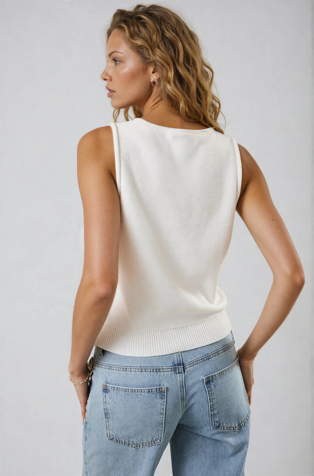 Woman wearing a white sleeveless top and blue jeans against a plain background