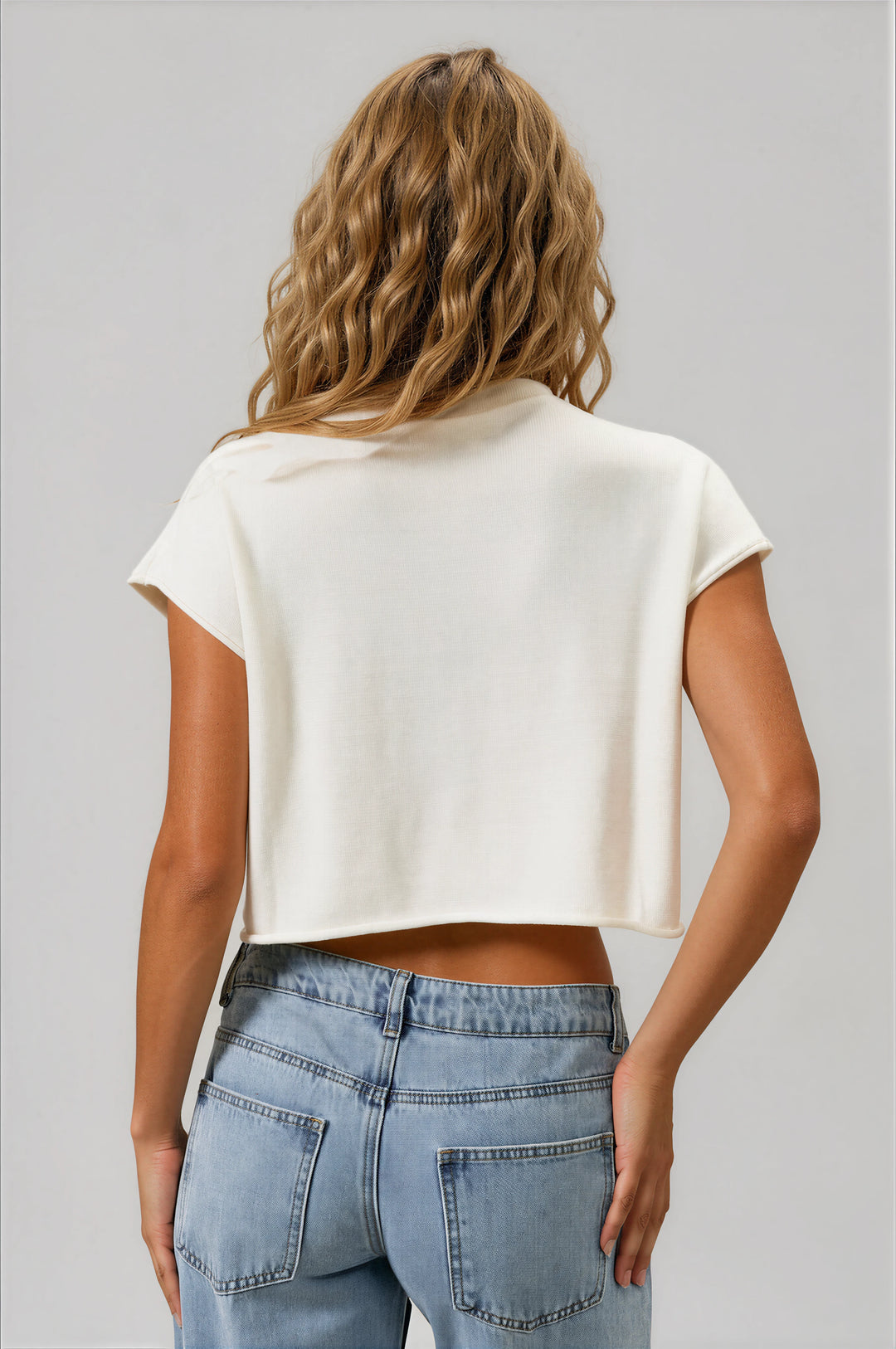 Person wearing a white crop top and blue jeans against a beige background