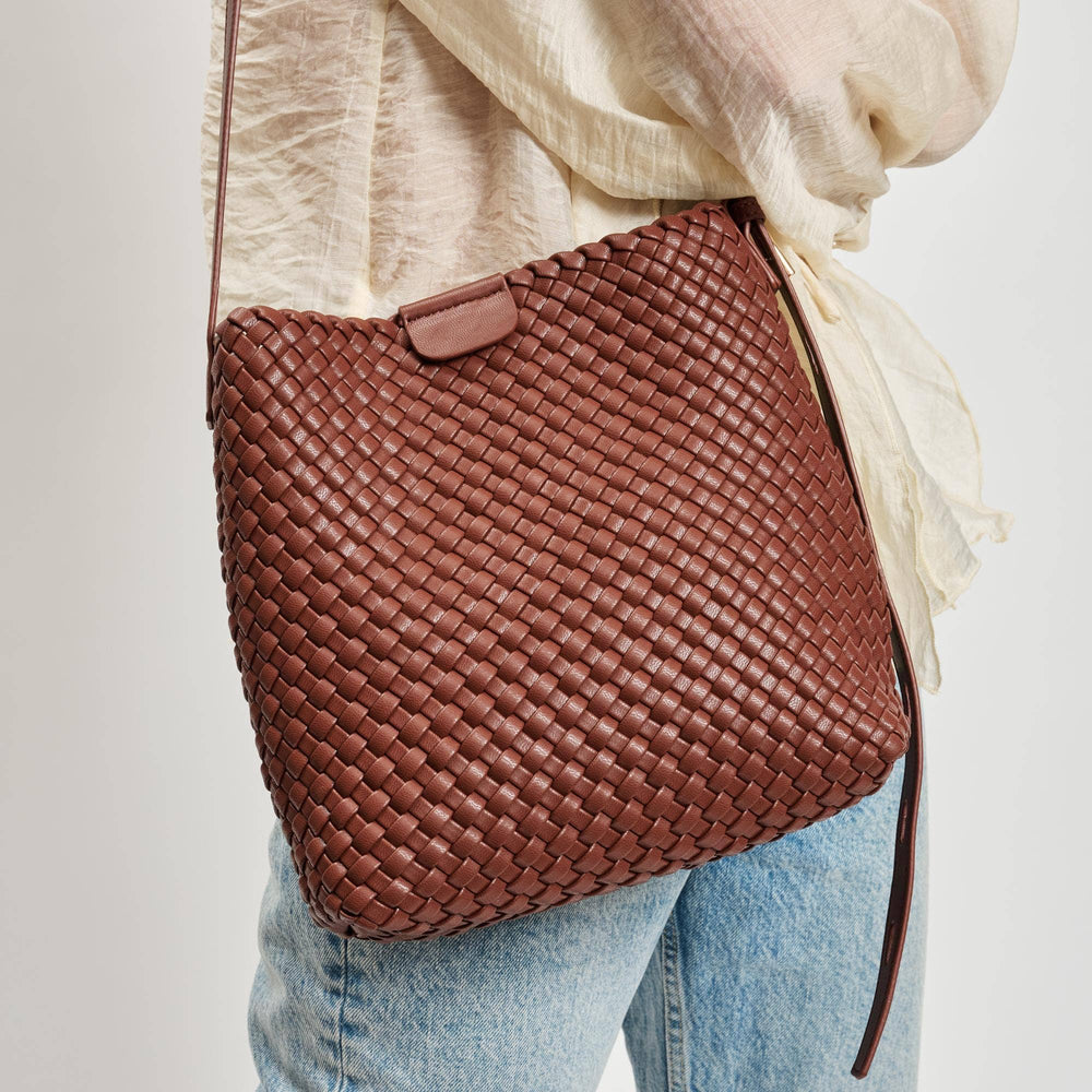 Brown woven handbag worn over shoulder with light-colored top and jeans