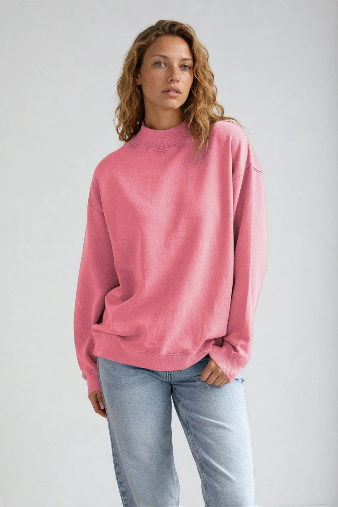 Woman wearing a pink sweater and light blue jeans against a plain background