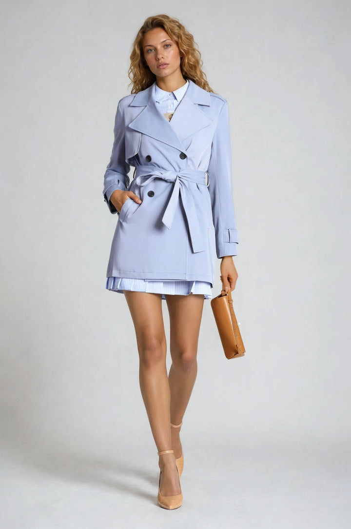 Woman wearing a light blue trench coat over a white dress on a plain background