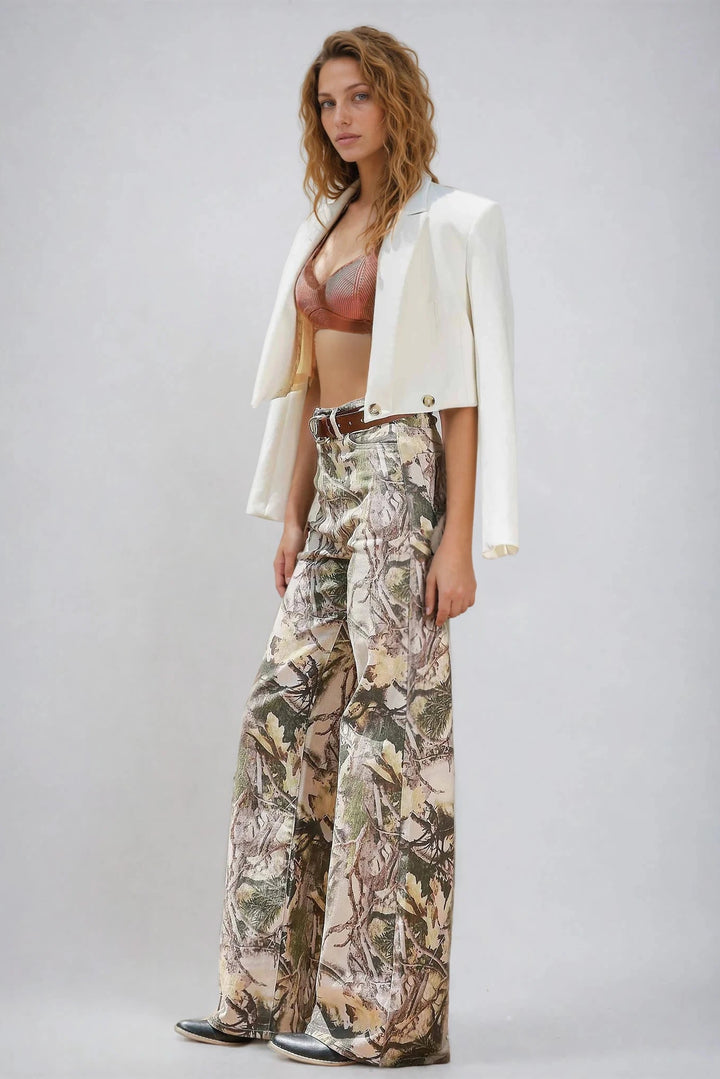 Woman wearing a white blazer, patterned pants, and a bralette on a plain background