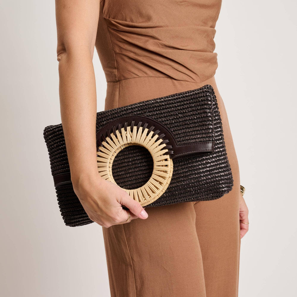 Person holding a black clutch with a woven design against a neutral background